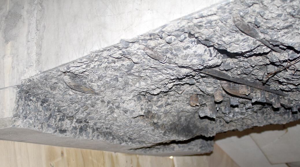 A concrete beam profiled by water with the aggregate and reinforcing exposed and the surrounding surface untouched