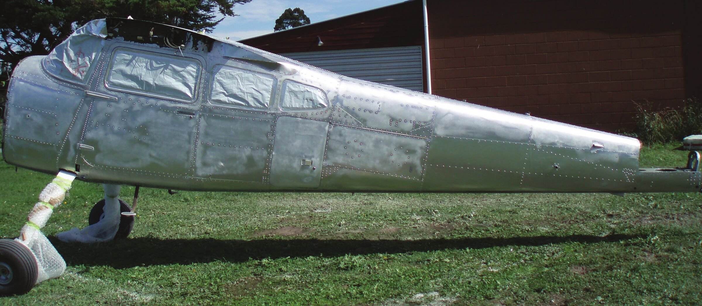 A Cessna 185 standing on grass with its paint removed back to bare aluminium