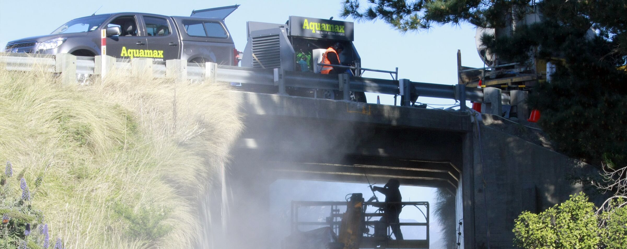 An Aquamax truck on the Kaikoura road overbridge with a white water jet throwing spray across the deck edge
