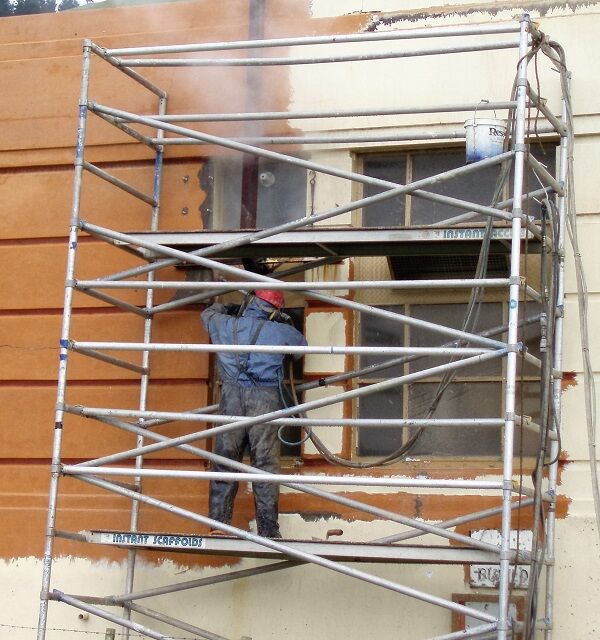 An operator on scaffolding washing down a masonry facade
