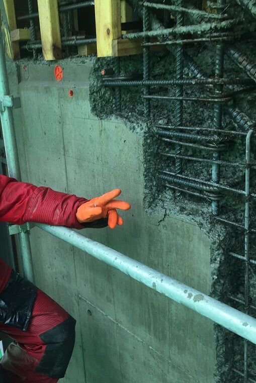 A gloved hand against a wall where water jetting has exposed the reinforcing steel