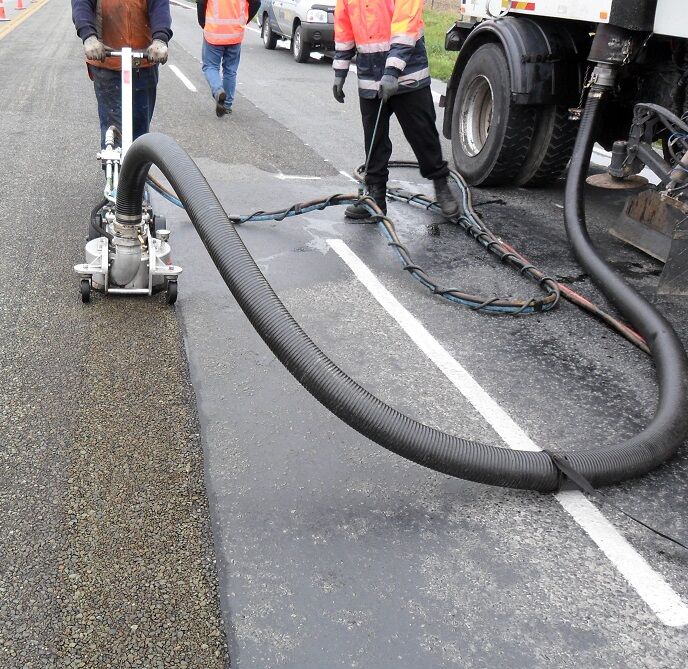 A crew dragging jetting hose across a road while removing line marking
