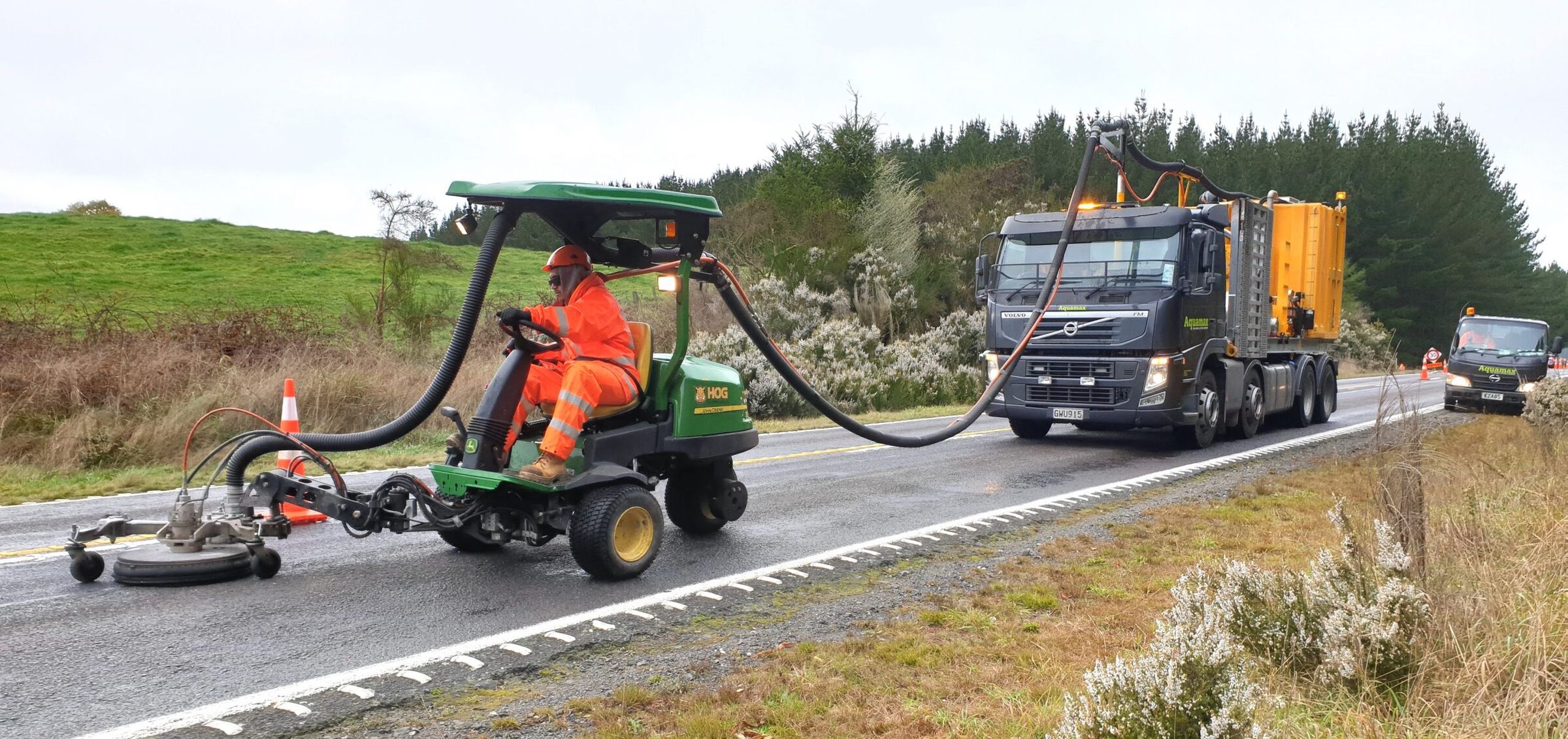 An operator on a ride-on removal head working a rural highway with a vacuum truck following